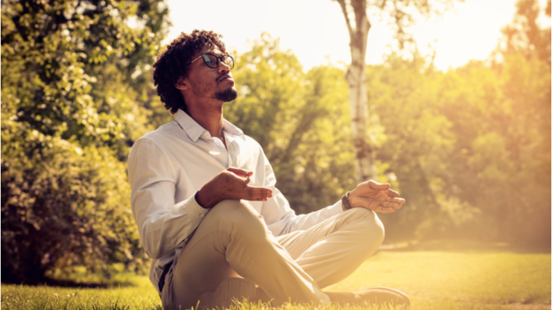 Man with glasses meditating in a lush green park