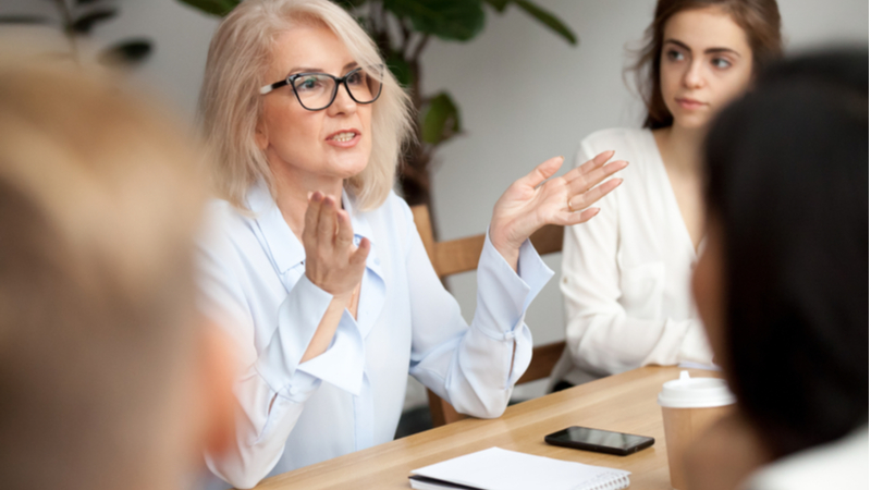 older woman with blonde hair and eyeglasses explaining details to her colleagues